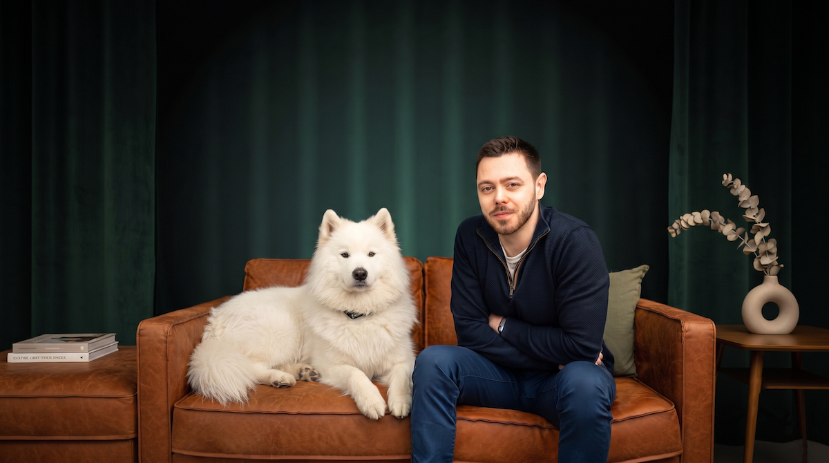 Valentin Quiskamp, Geschäftsführer von QUCOMM // MARKETING, sitzt mit einem weißen Samojeden auf einem Ledersofa